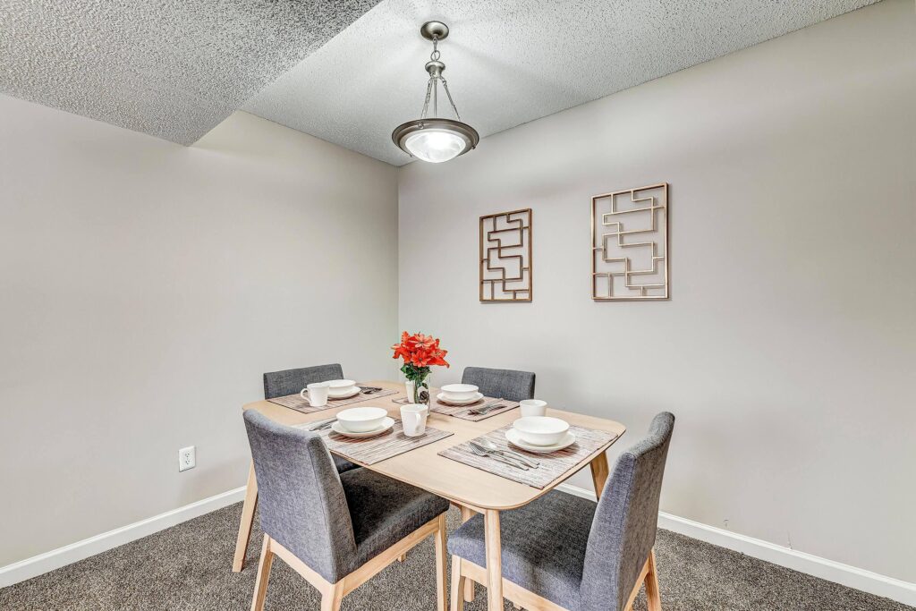 A small dining table set for four with gray chairs, white dishes, a flower centerpiece, and geometric wall art in a minimalist dining room.