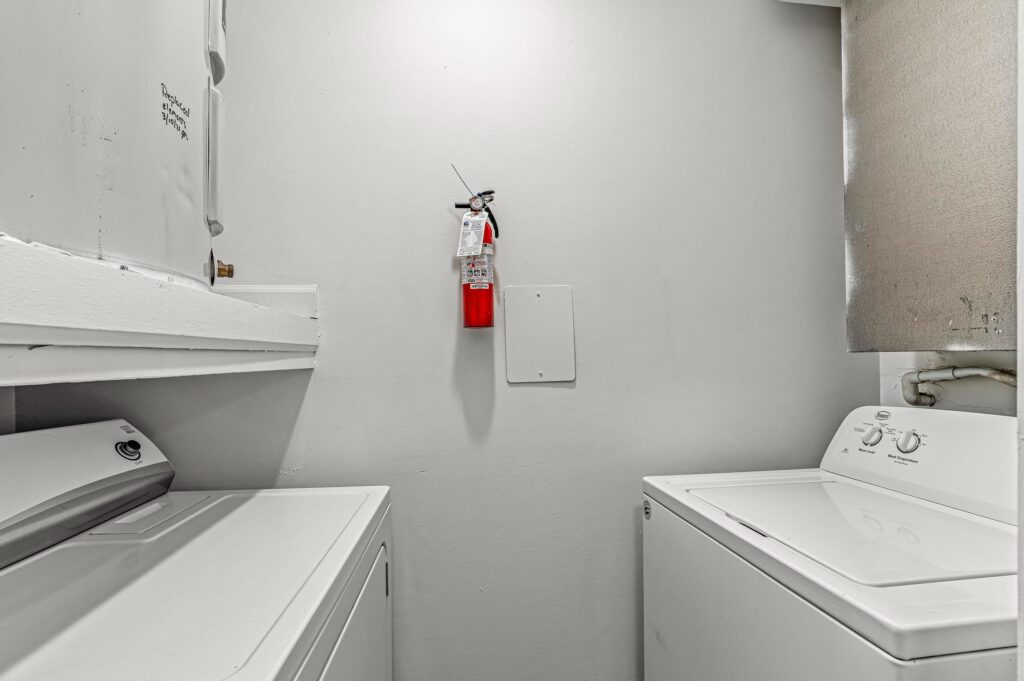 A small laundry room with a washing machine, dryer, and a fire extinguisher mounted on the white wall.