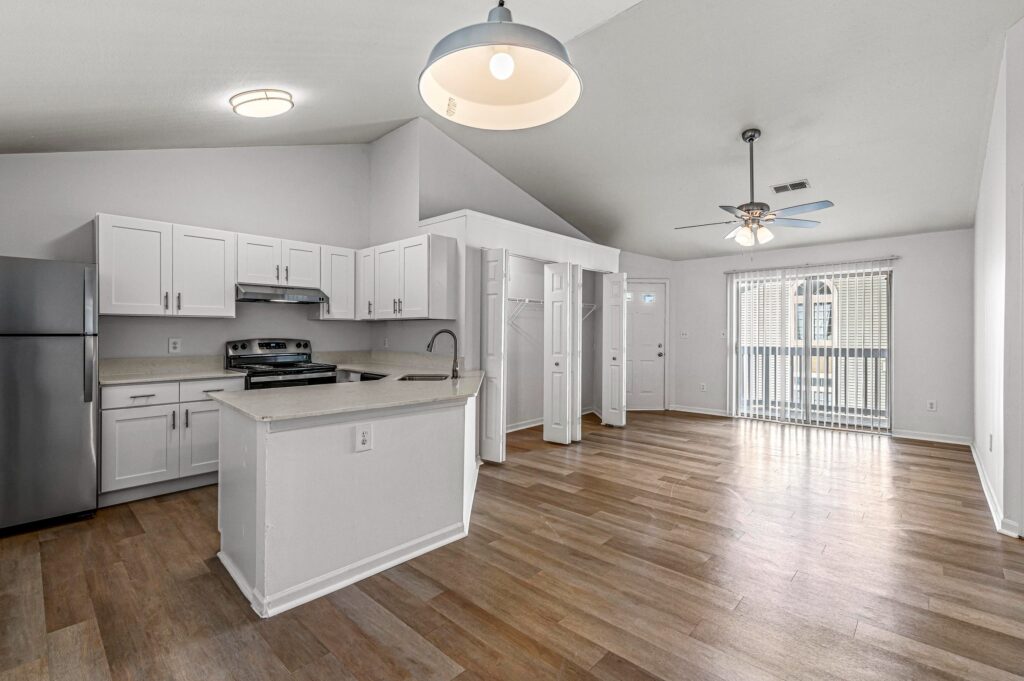 Modern kitchen and living area with white cabinets, stainless steel appliances, island, wood flooring, ceiling fan, and sliding glass door leading to a balcony.