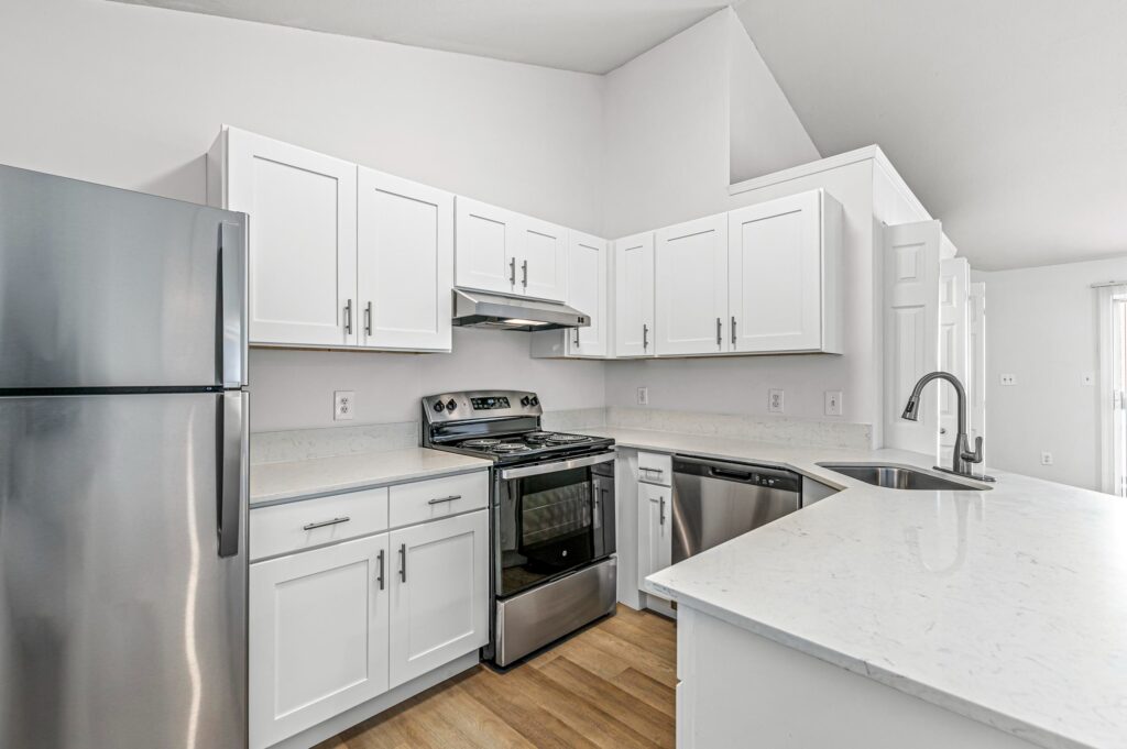 Modern kitchen with white cabinets, stainless steel appliances, electric stove, and a double sink set in a white marble countertop, with light wood flooring.