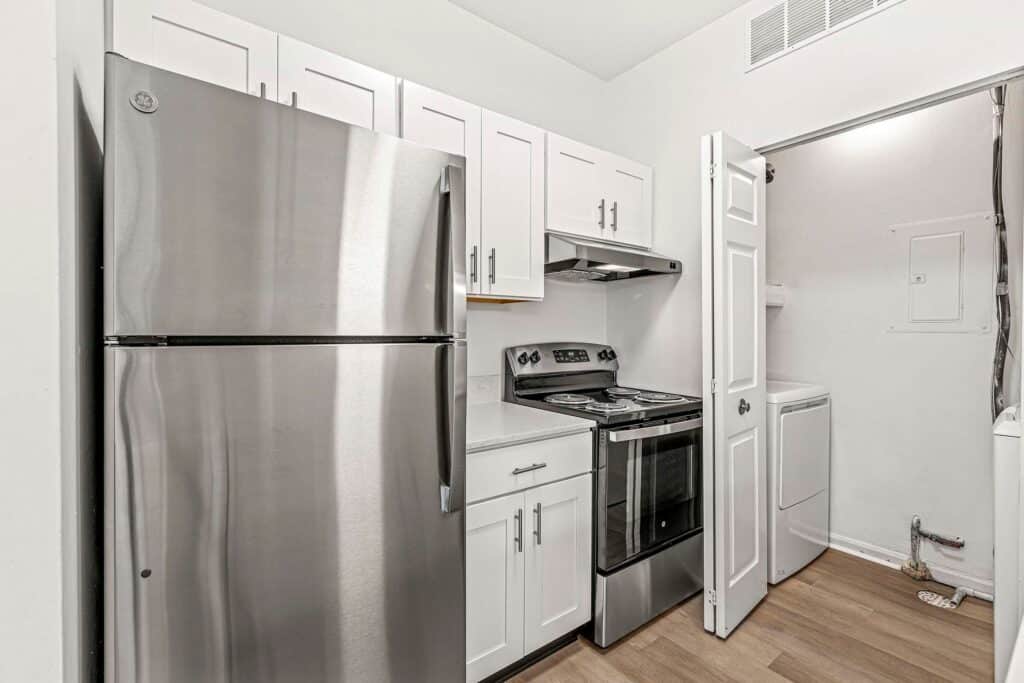 Modern kitchen with stainless steel refrigerator, electric stove, white cabinets, and an adjacent laundry area with a washer and dryer.