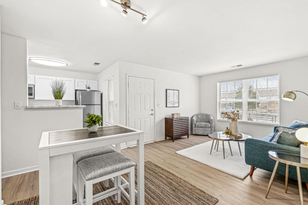 Modern, bright Arborwood Apartments interior with open kitchen, small dining table, cozy living area, large window, light wood flooring, and minimal decor.