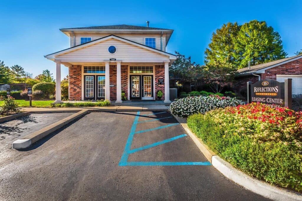 A brick building with white columns, landscaped bushes, and a "Leasing Center" sign, with handicap parking in front.