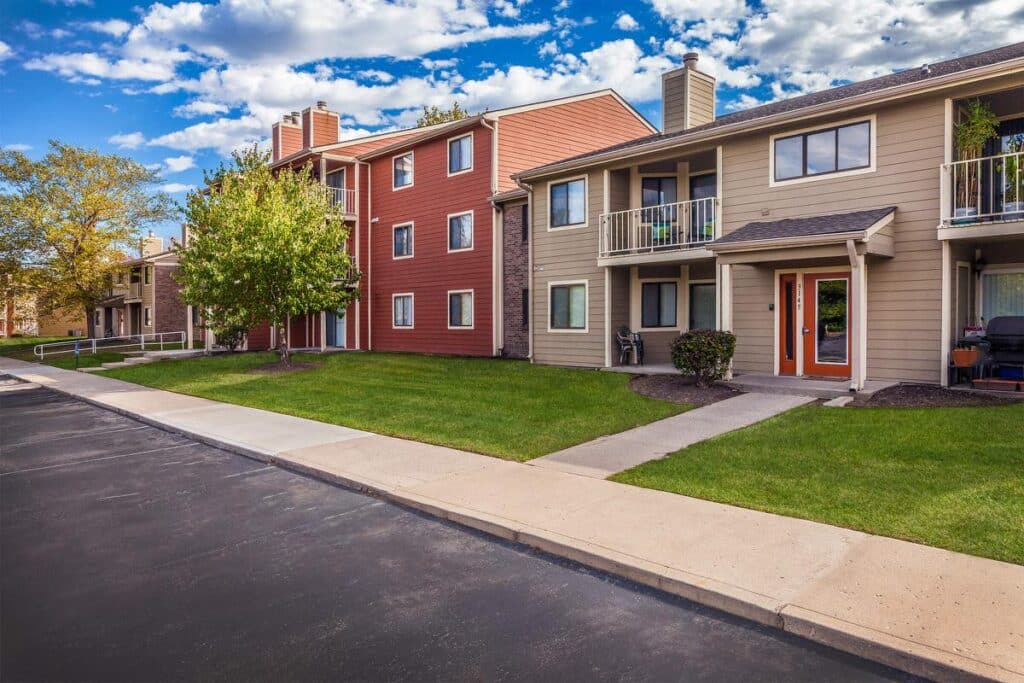 Three-story and two-story Villages of Bent Tree Apartments with balconies and green lawns line a paved roadway under a partly cloudy sky.
