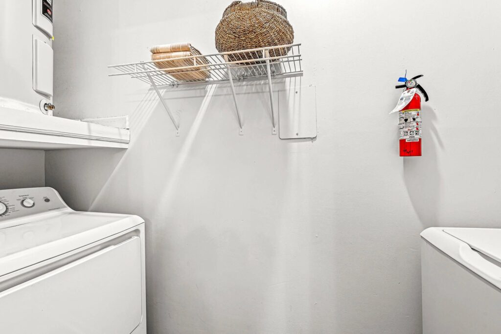 Laundry room with a washer and dryer, a wall-mounted wire shelf holding towels and a basket, and a fire extinguisher on the wall.