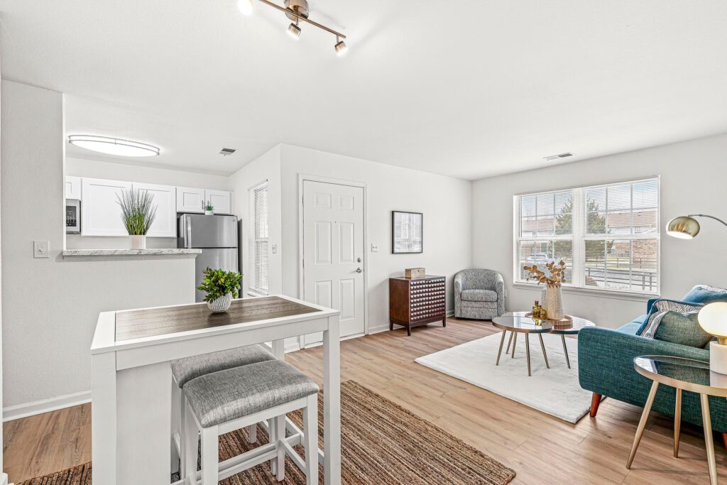 Bright, modern living space with a small dining table, kitchenette, seating area, large window, and neutral decor.