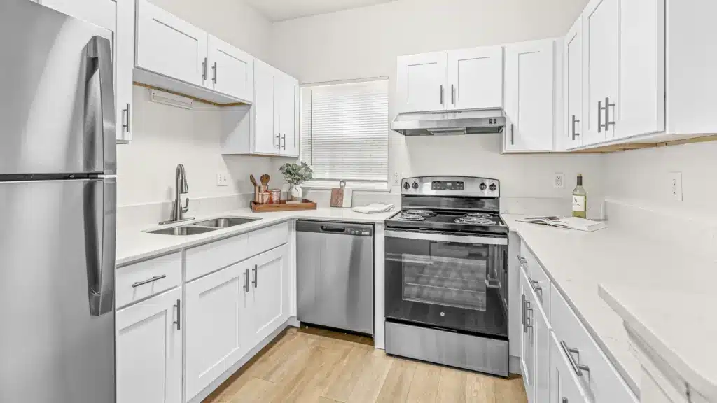 Modern kitchen with white cabinets, stainless steel appliances, electric stove, dishwasher, refrigerator, and a window above the sink. Countertops are white with minimal decor.