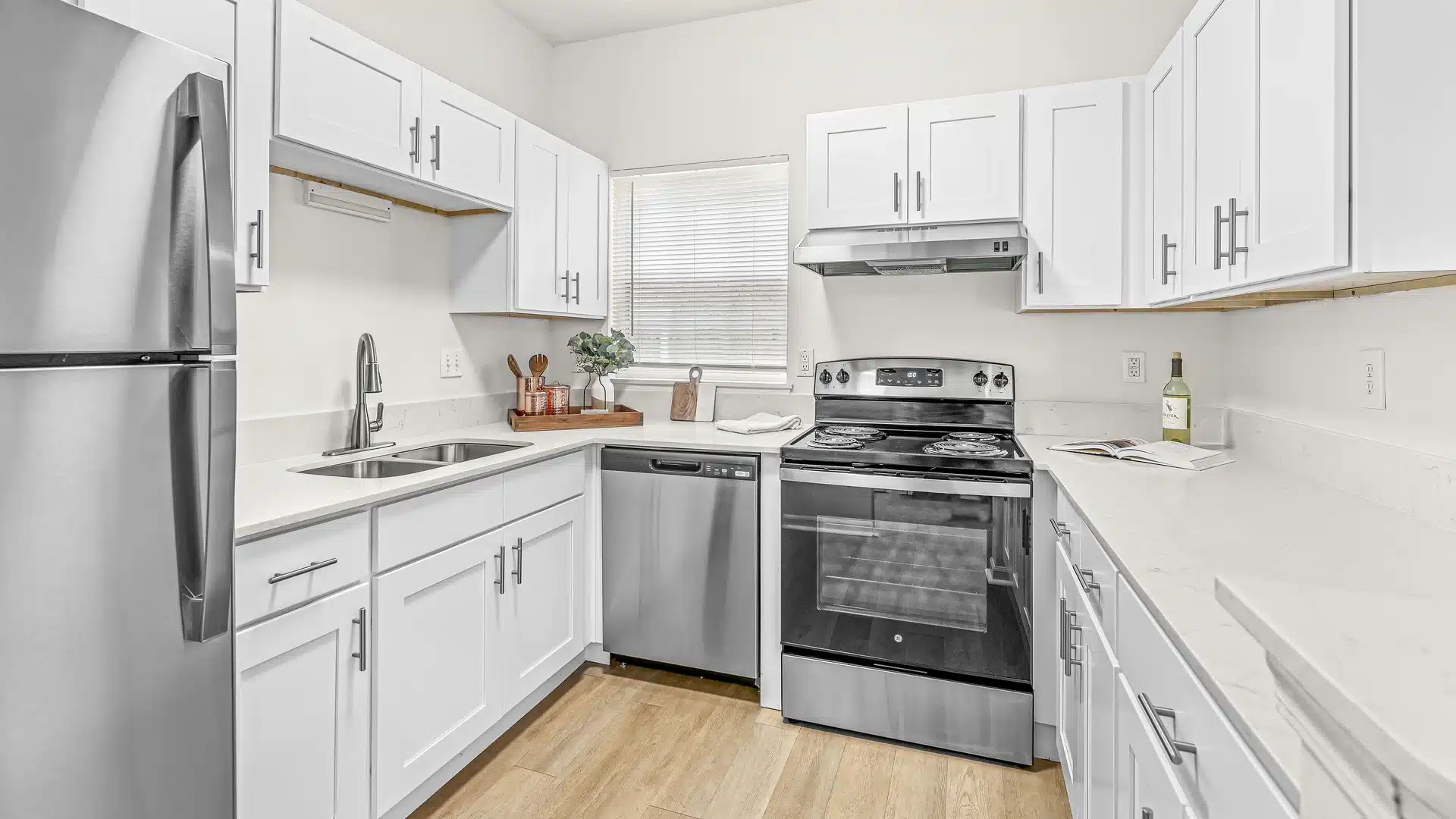 Modern kitchen with white cabinets, stainless steel appliances, electric stove, dishwasher, refrigerator, and a window above the sink. Countertops are white with minimal decor.