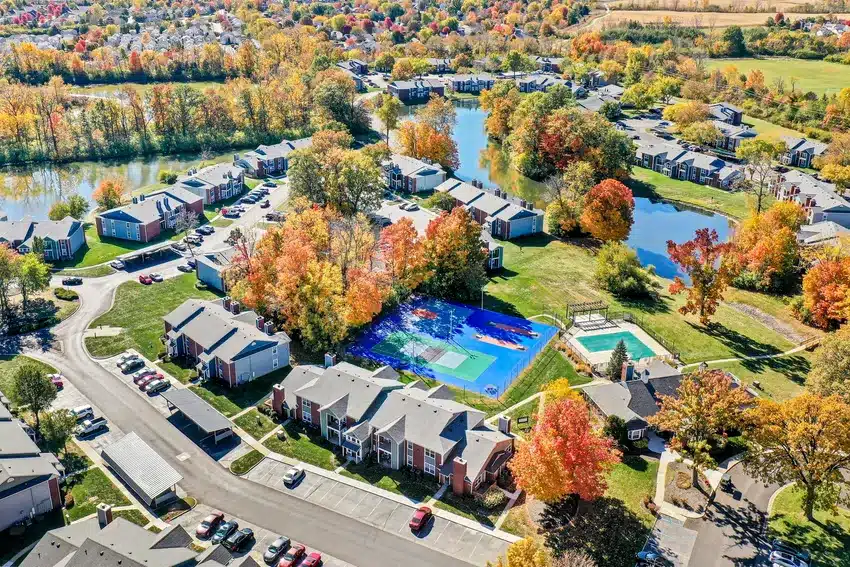 Aerial view of a residential neighborhood with apartment buildings, colorful autumn trees, a blue sports court, outdoor pool, and several small lakes.