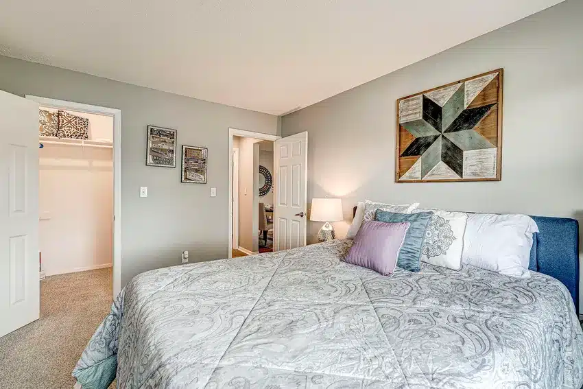 A bedroom with a neatly made bed, patterned bedding, decorative pillows, wall art above the headboard, and an open door leading to a walk-in closet.