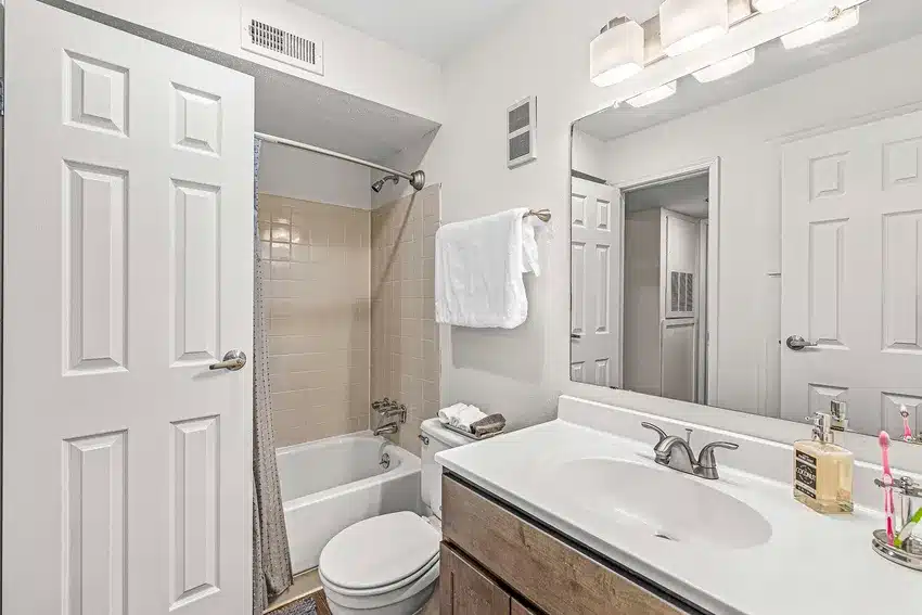 Modern bathroom with a bathtub-shower combo, toilet, white countertop sink, large mirror, towel rack, and overhead lighting.