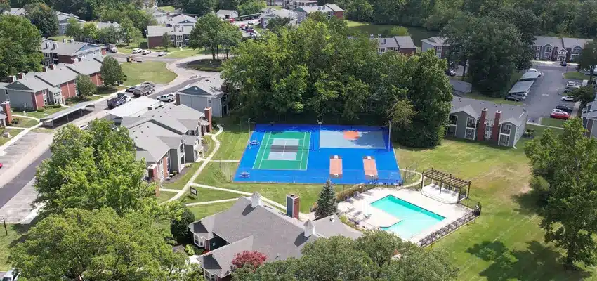 Aerial view of a residential complex with tennis and basketball courts, a swimming pool, surrounding lawns, and multiple apartment buildings.
