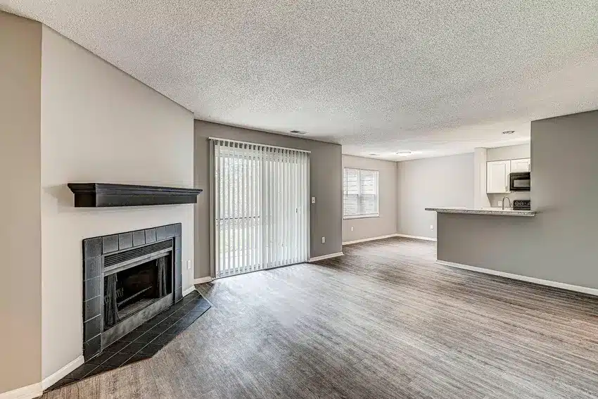 Open living area with a black-tiled fireplace, wood flooring, sliding glass doors, and a view of the kitchen with a breakfast bar.