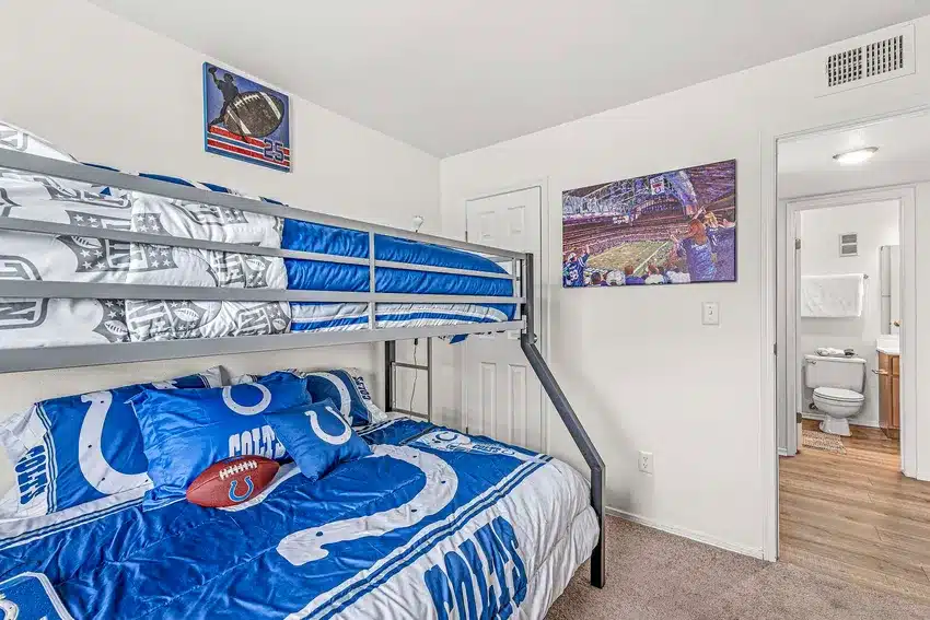 A bedroom with a Colts-themed bunk bed, sports decor on the walls, carpet flooring, and an open door showing a bathroom with wood-style flooring.