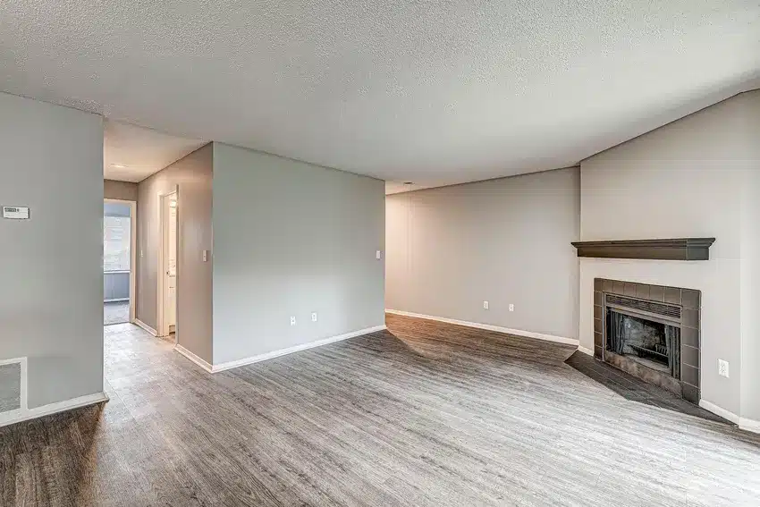 Unfurnished living room with gray walls, wood-look flooring, and a dark-framed fireplace. An open doorway leads to a hallway and another room.