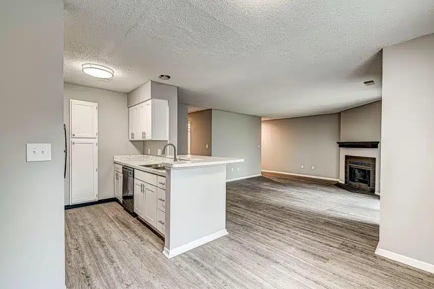 Open-plan living area with gray flooring, a modern white kitchen with marble countertops, and a fireplace in the corner of the living room.