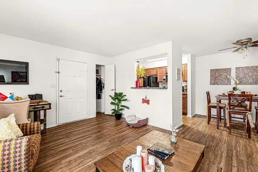 A living room with wood flooring, open closet, and visible kitchen and dining area, furnished with a sofa, coffee table, and indoor plant.