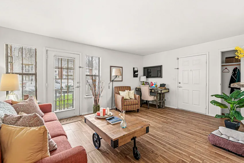 A bright living room with wood floors, a red sofa, a rolling coffee table, and a workspace in the corner near a windowed door.