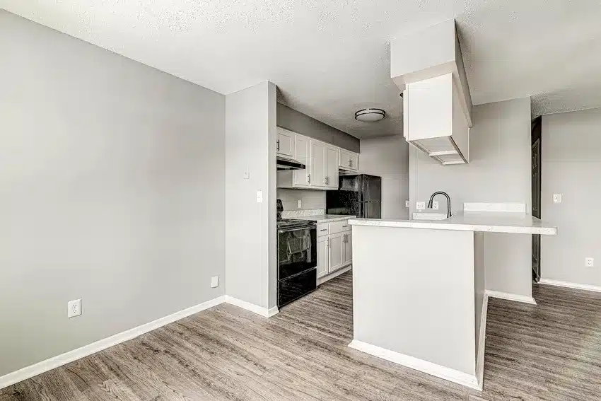Modern kitchen with light gray walls, white cabinets, stainless steel appliances, and a small peninsula with a sink, featuring wood-look flooring.