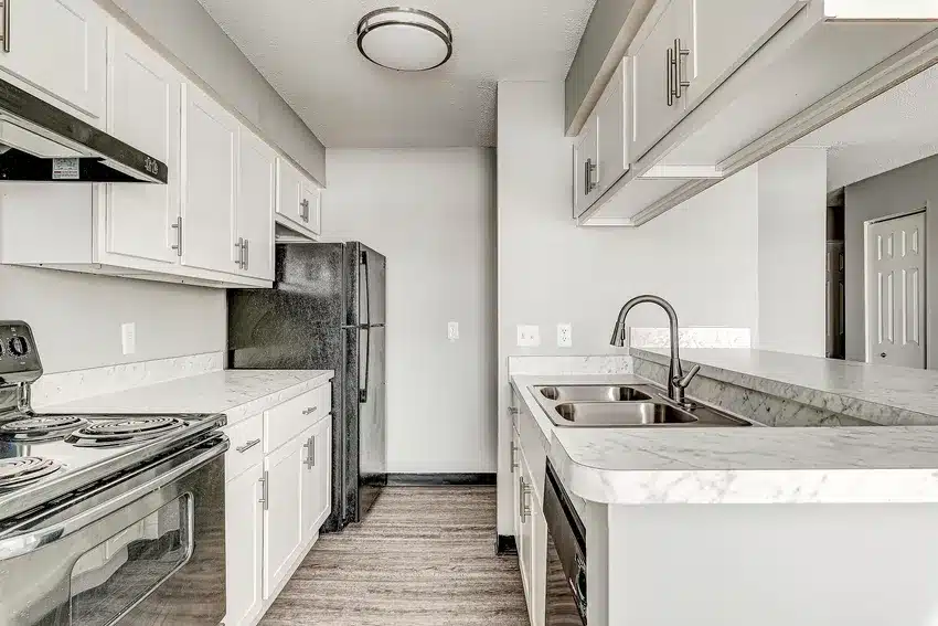 Modern kitchen with white cabinets, marble countertops, stainless steel sink, black appliances, and wood-style flooring.