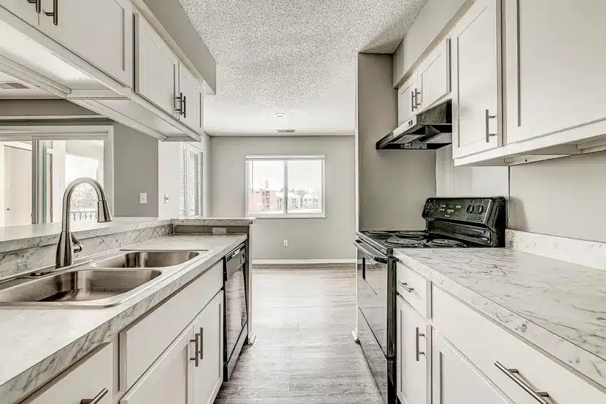 Modern kitchen with white cabinets, marble countertops, stainless steel sink, black stove, dishwasher, and large window with natural light.