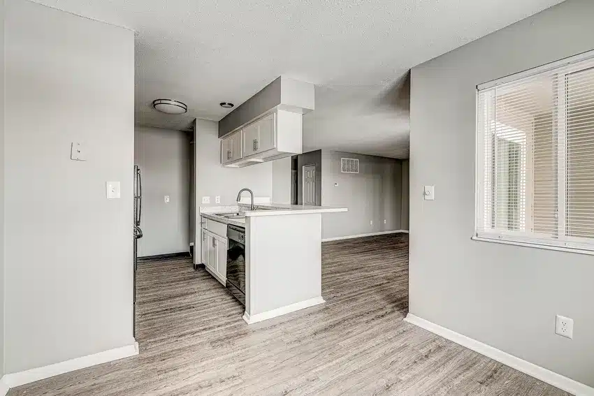 Modern kitchen with light gray walls, wood-style flooring, white countertops, stainless steel appliances, and a large window with blinds.