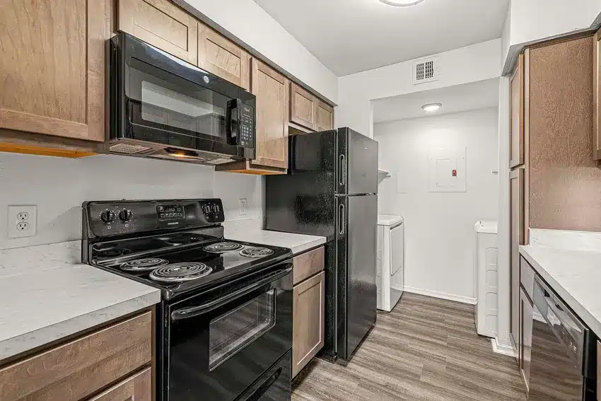 A kitchen with black appliances, brown cabinets, white countertops, and a visible washer and dryer in a laundry area at the back.