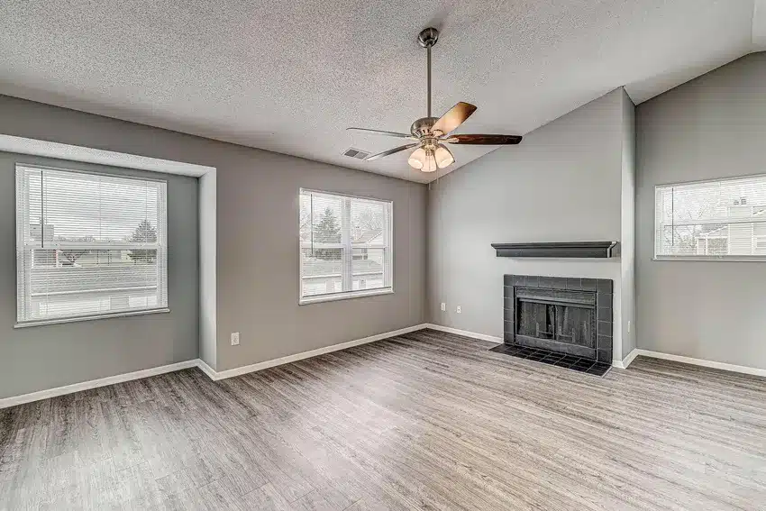 Unfurnished living room with gray walls, wood flooring, a ceiling fan with lights, large windows, and a black fireplace.