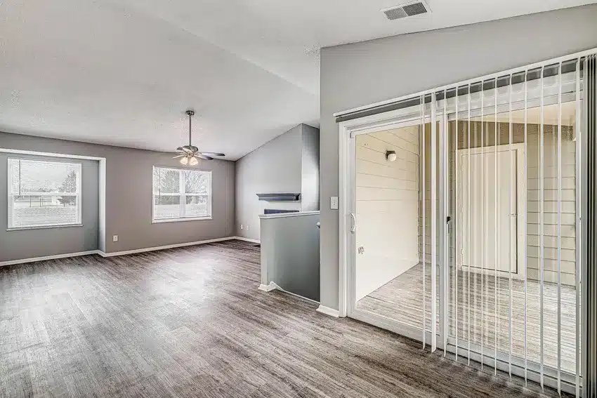 Spacious living area with large windows, ceiling fan, light wood flooring, gray walls, and sliding glass door leading to an enclosed patio.