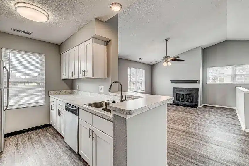 Modern kitchen with white cabinets and stainless steel appliances opens to a living area with wood-style flooring, vaulted ceiling, and a fireplace.