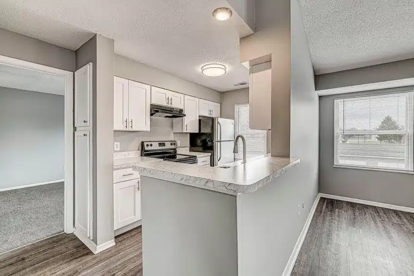 Modern kitchen with white cabinets, stainless steel appliances, marble-look countertops, and a pass-through to a bright dining area with large windows.