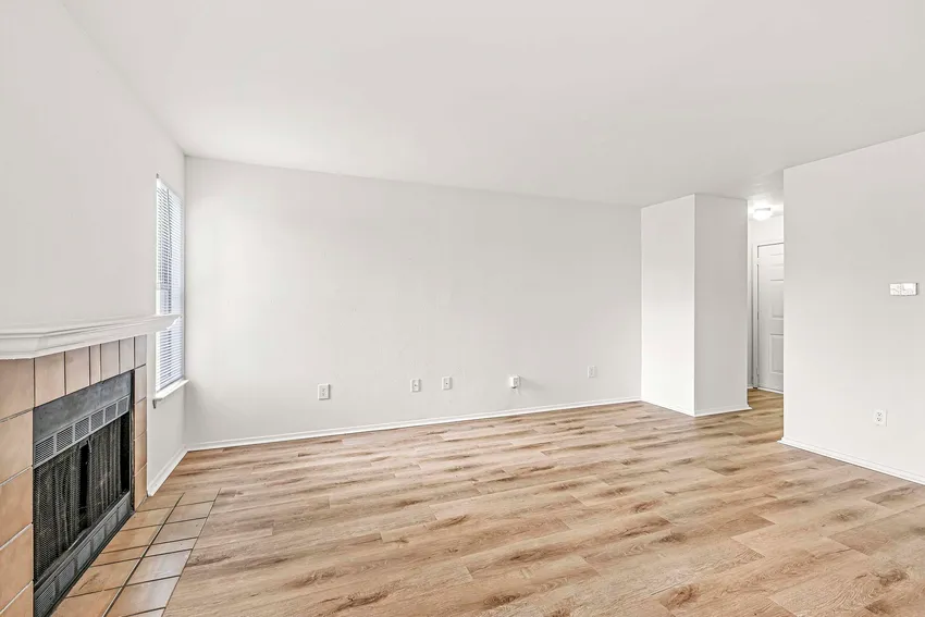 Unfurnished living room with light wood flooring, a white wall, a window, and a fireplace with a tiled hearth.