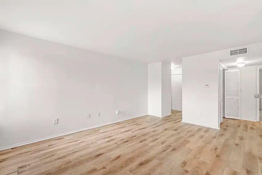 Empty room with white walls, light wood flooring, ceiling vent, and doors leading to other areas, including a closet with louvered doors.