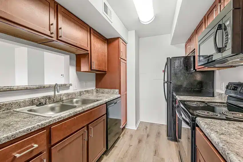 Modern kitchen with wood cabinets, granite-style countertops, double sink, black appliances including fridge, dishwasher, stove, and microwave, and wood flooring.