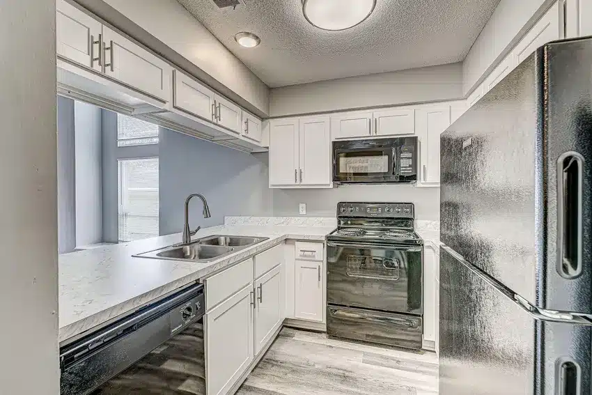 Modern kitchen with white cabinets, marble countertops, stainless steel sink, black appliances, and light wood flooring.