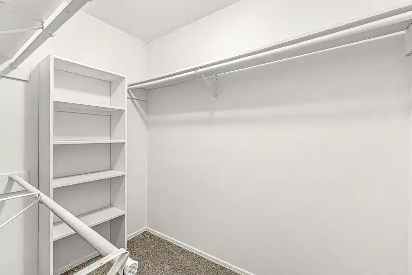 Empty walk-in closet with white walls, built-in shelves, carpeted floor, and multiple hanging rods.