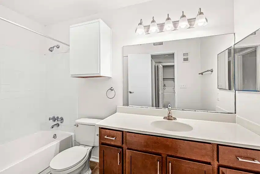 Modern bathroom with a bathtub-shower combo, toilet, large mirror, white countertop, dark wood vanity, and overhead light fixture.
