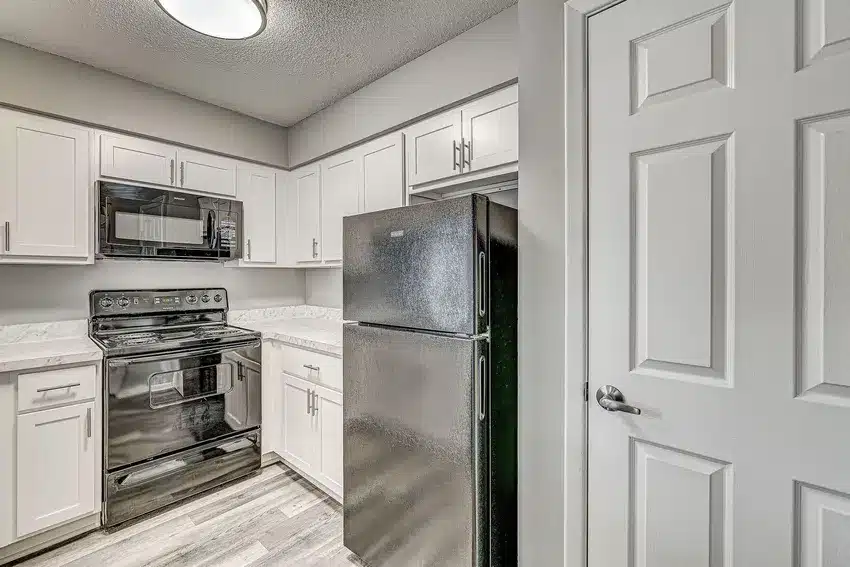 Modern kitchen with stainless steel refrigerator and black stove, white cabinets, marble-look countertops, and gray wood flooring.