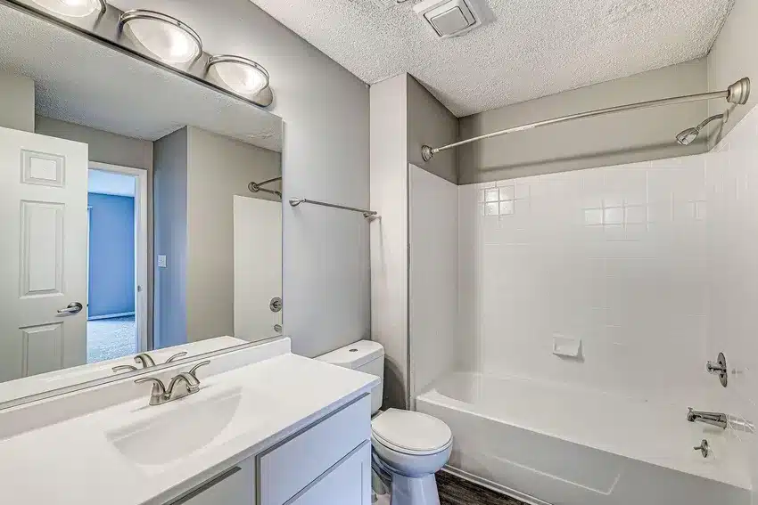 Modern bathroom with white vanity, mirror, toilet, and bathtub-shower combo; neutral wall color and overhead lighting.