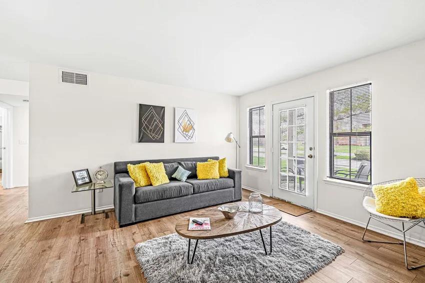 A bright living room with a gray sofa, yellow pillows, two modern wall art pieces, a coffee table on a gray rug, and windows letting in natural light.