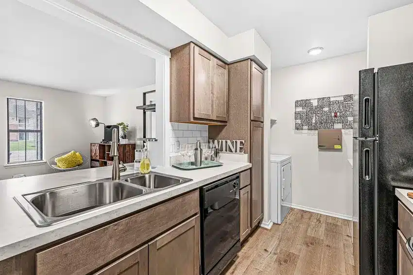Modern kitchen with wood cabinets, double sink, black appliances, and white countertops; laundry area with washer and dryer in the back.
