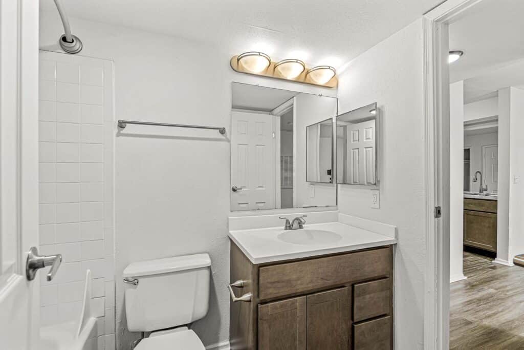 Modern bathroom with a single sink vanity, wood cabinet, wall mirror, toilet, towel rack, and a white tiled shower area.
