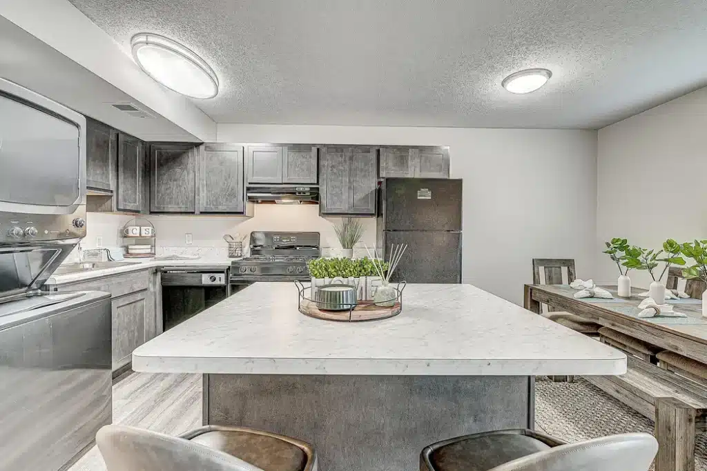Modern kitchen with gray cabinets, marble island, stainless steel appliances, and adjacent dining area with a wooden table set for four.