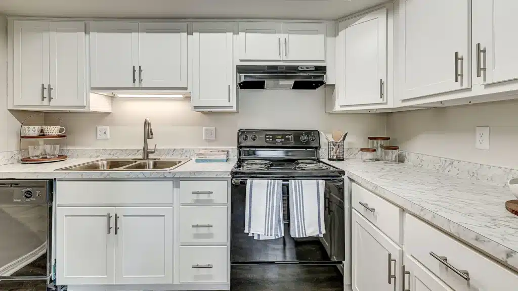 A modern kitchen with white cabinets, marble countertops, a black stove with striped towels, a sink, and stainless steel dishwasher.
