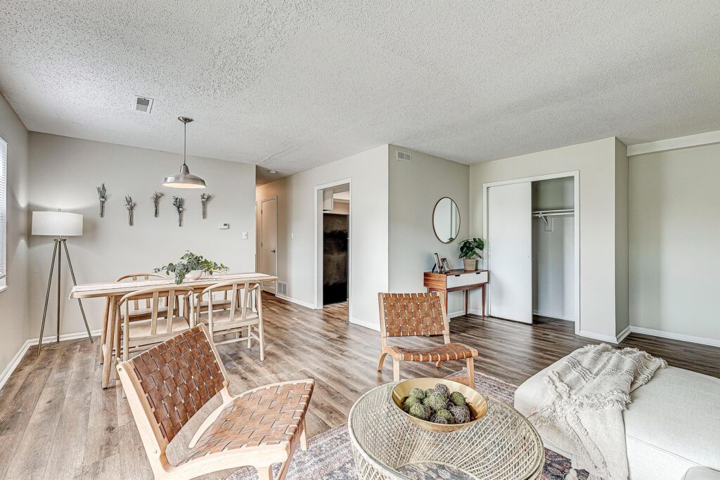 A modern living and dining area with wood flooring, neutral walls, woven chairs, a dining table, and a small desk with a round mirror.