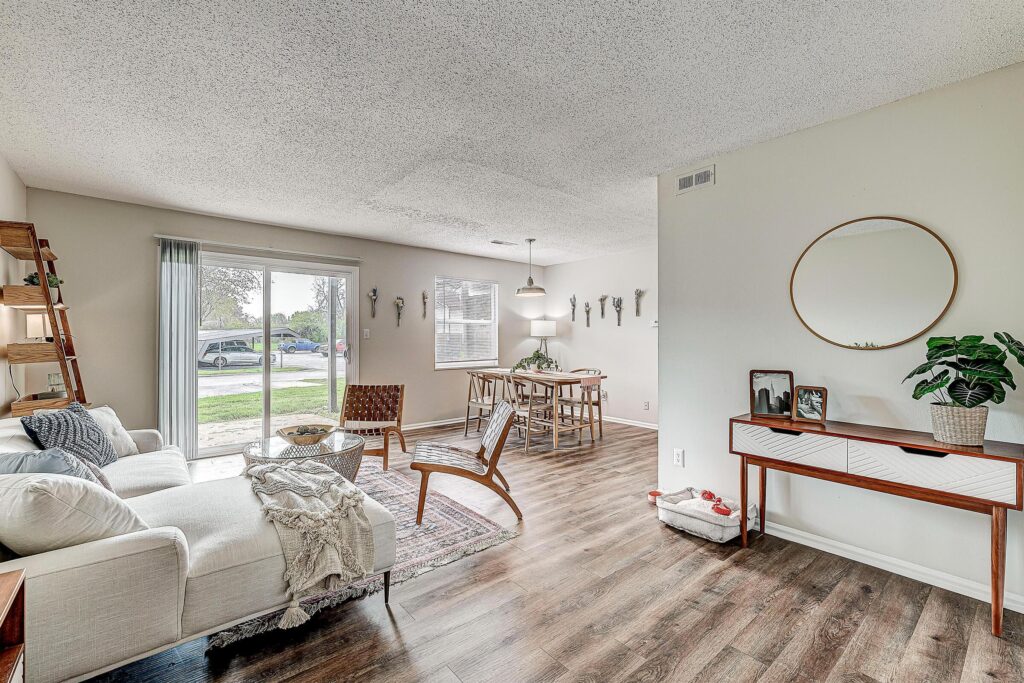 A modern living and dining area with wood flooring, white walls, a sofa, a dining table, and large windows letting in natural light.