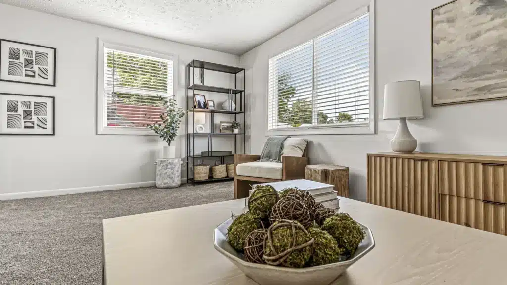Modern living room with neutral decor, a bowl of decorative moss balls on a wooden coffee table, and large windows letting in natural light.