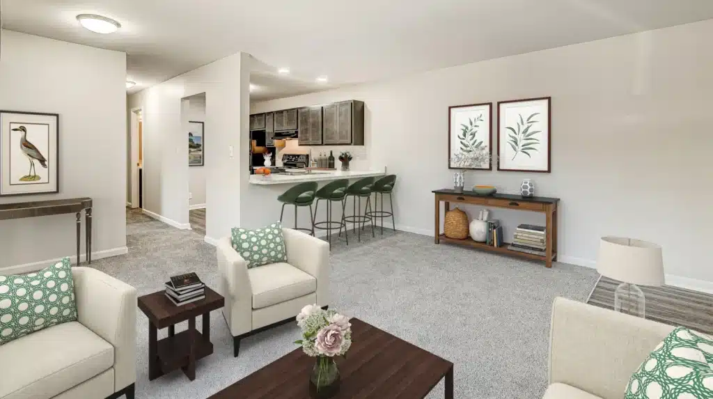 Modern open-plan living room with light carpet, beige armchairs, a wooden coffee table, kitchen with bar stools, and botanical artwork on the wall.
