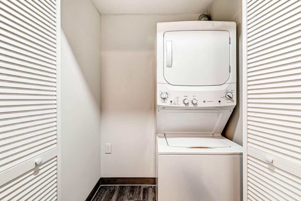 A small laundry closet with white bi-fold doors contains a stacked washer and dryer unit against the back wall.