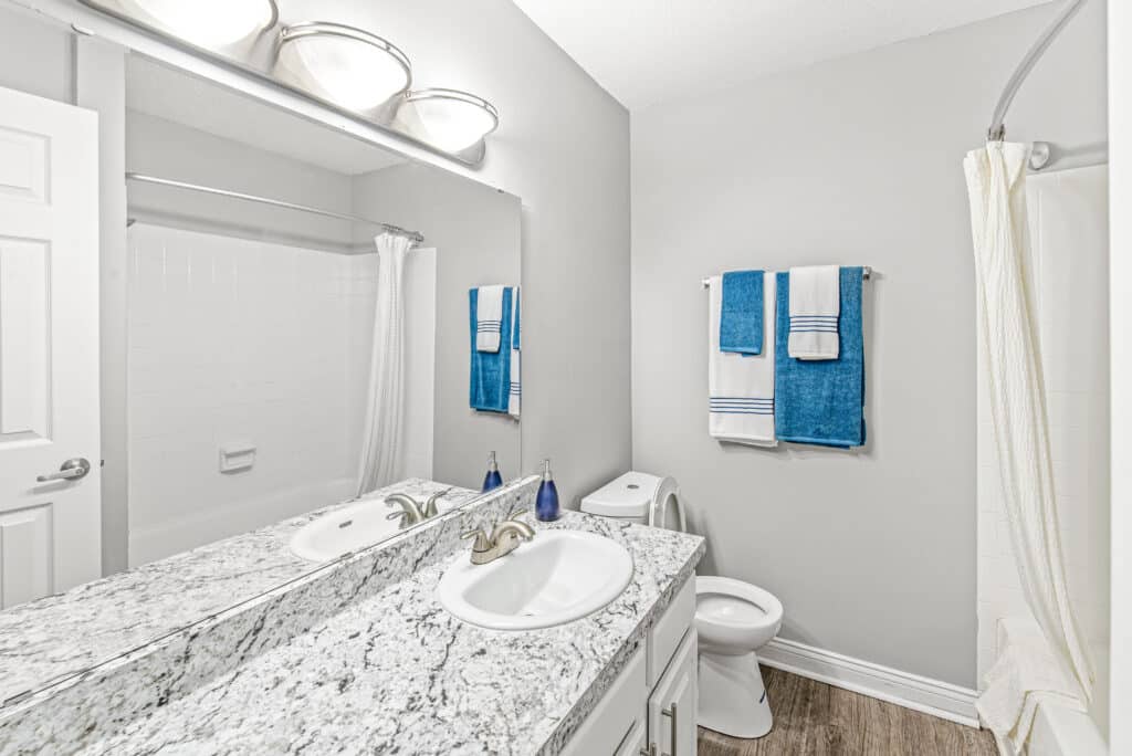 Modern bathroom with a granite countertop, double sinks, a toilet, a shower with a curtain, and blue and white towels hanging on the wall.